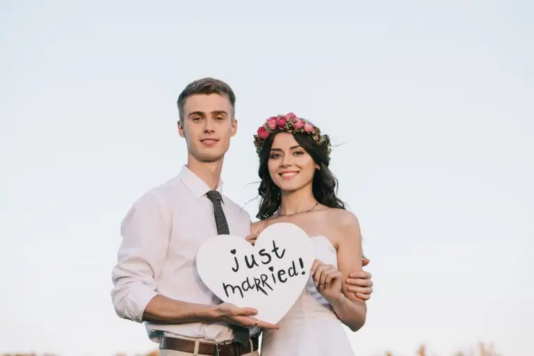 happy young wedding couple holding heart with just married inscription and smiling at camera